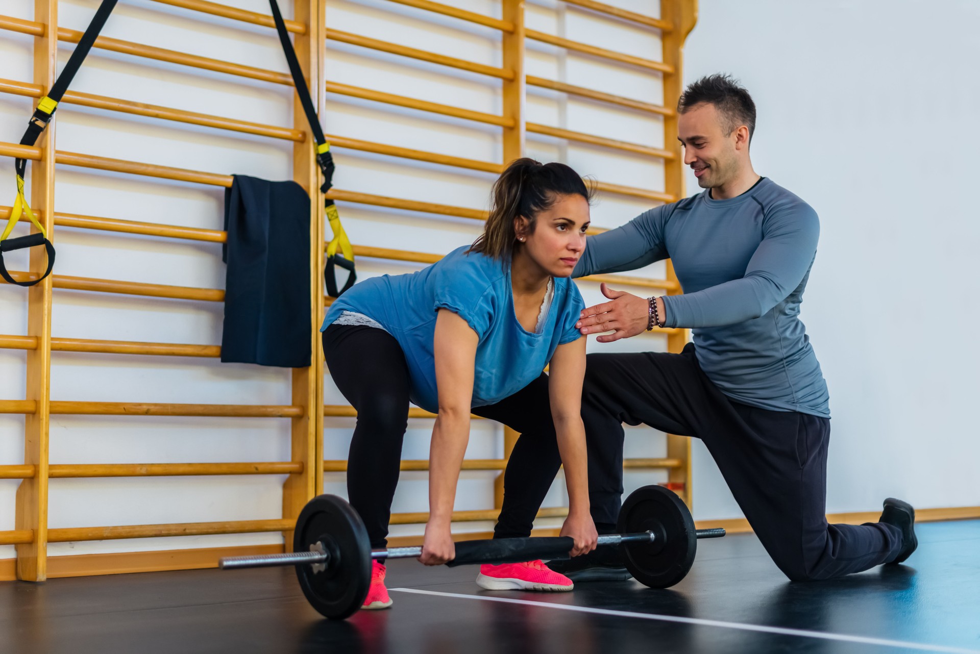 couple of a smiling personal trainer and a beautiful pregnant woman doing workout exercise indoor.girl lifting weight in a gym session inside. fit,training,fitness,health and friendship concept