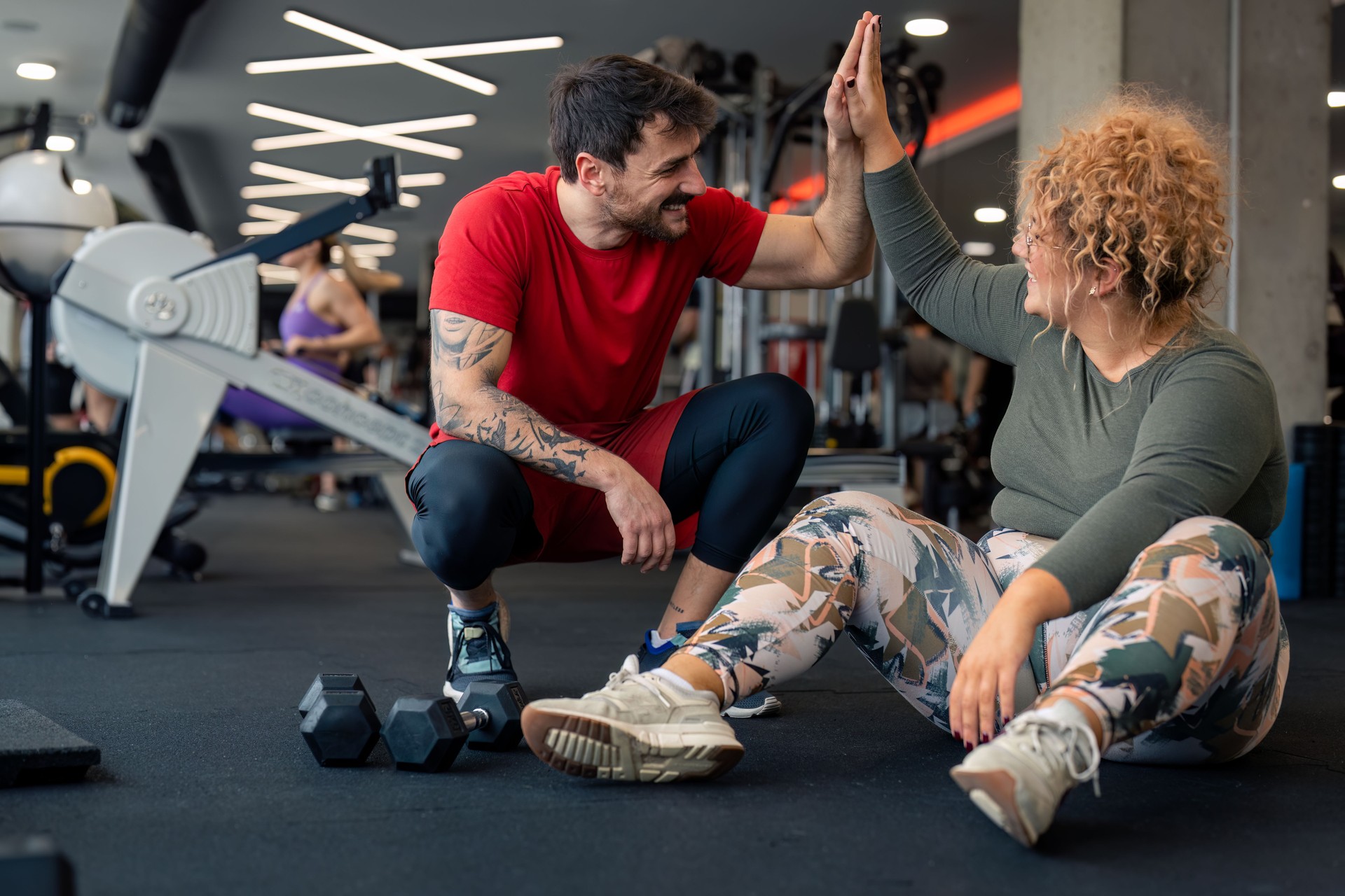 Happy male coach giving young woman high-five after successful sports training session in gym